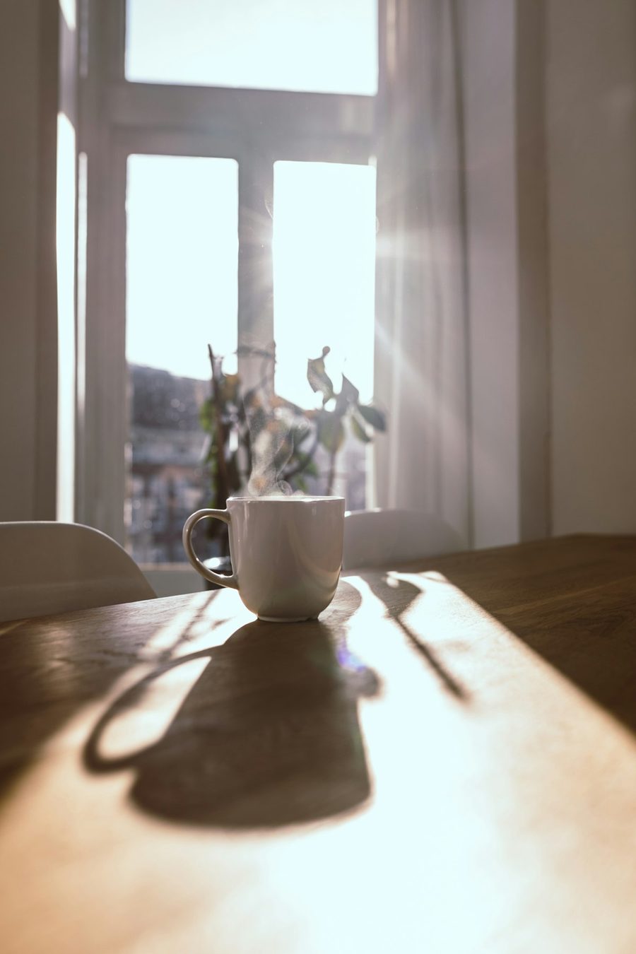 A steaming mug on a wooden table in bright morning sunlight